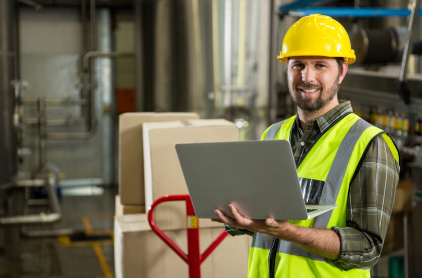 Portrait of smiling male worker using laptop in distribution warehouse